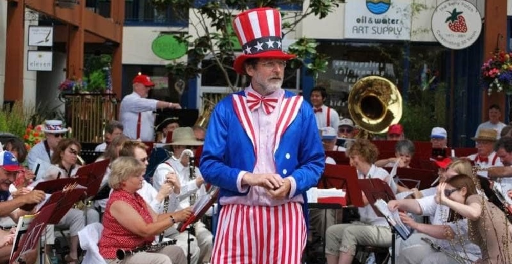 A man wearing a red, blue and white hat, pants and jackets with a band behind him