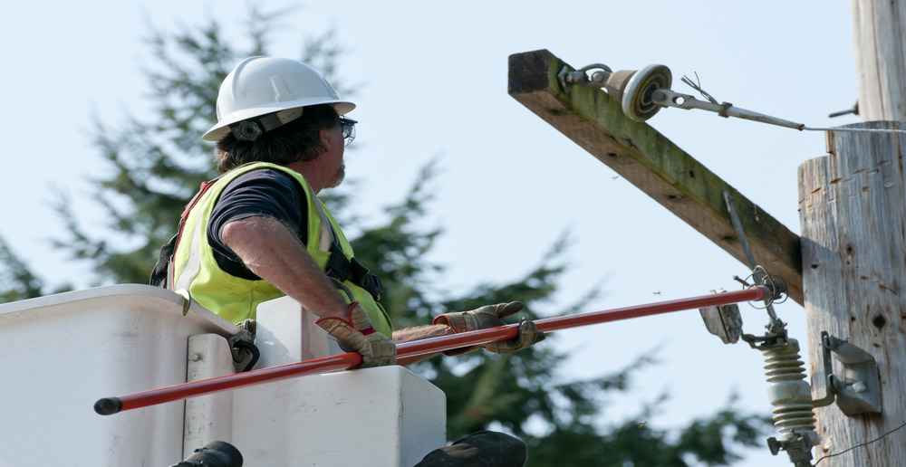 Construction worker in boom lift uses a tool to adjust equipment on electrical pole.